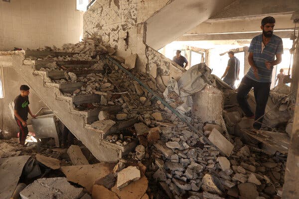 Four men look around a staircase covered in rubble, in a building where the walls have been blown away.