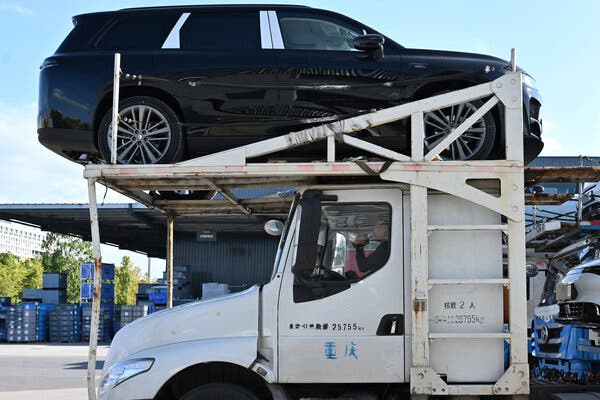 A white car carrier with a dark S.U.V. above the driver's cab.