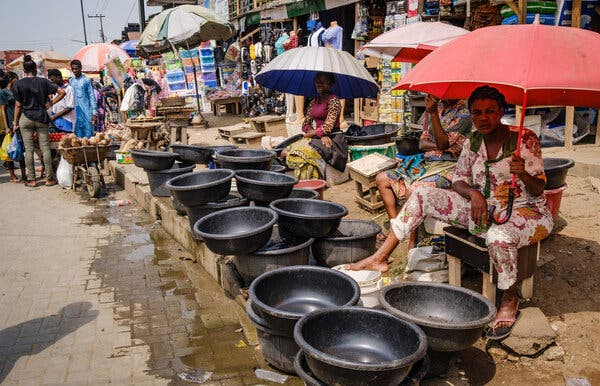 Women sitting under umbrellas behind rows of stacked black pots.