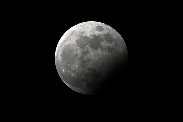 The moon, partially obscured by a lunar eclipse, in the night sky.