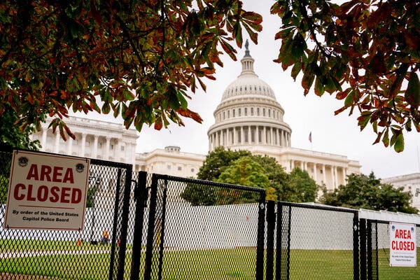 The U.S. Capitol building is framed by red and green leaves on a tree, with a black fence in the foreground noting the area is closed to the public.