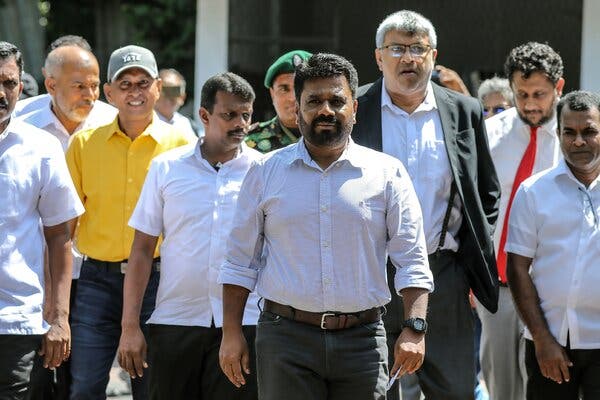 A bearded man in a white shirt walks amid a crowd of other men outdoors.