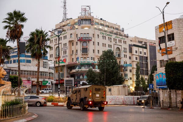 A military vehicle in front of a multistory building on a city street.