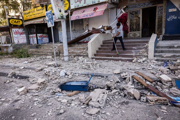 A man sweeps up steps outside a building on an urban street as chunks of concrete lie in front.