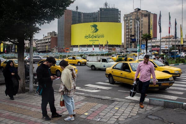 A large yellow billboard on a tower block, displaying a stylized portrait of Hassan Nasrallah above a Quranic quotation.