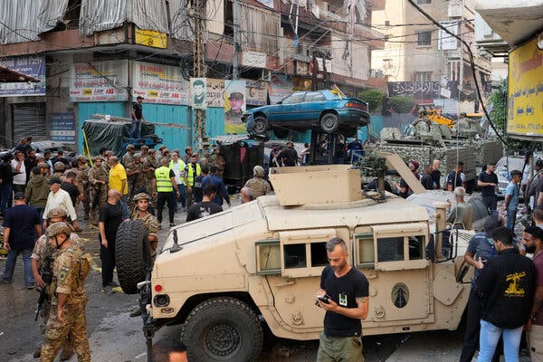 People on a crowded street after an airstrike. A forklift  is removing a damaged car.