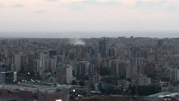 A cityscape against a gray sky as smoke billows above a building. 