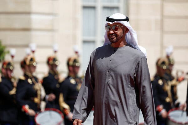 Sheikh Mohammed bin Zayed wearing a gray tunic, white head scarf, and sunglasses.