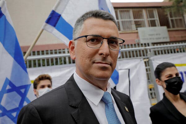 A man wearing a gray suit, a blue tie and glasses looks toward the camera.