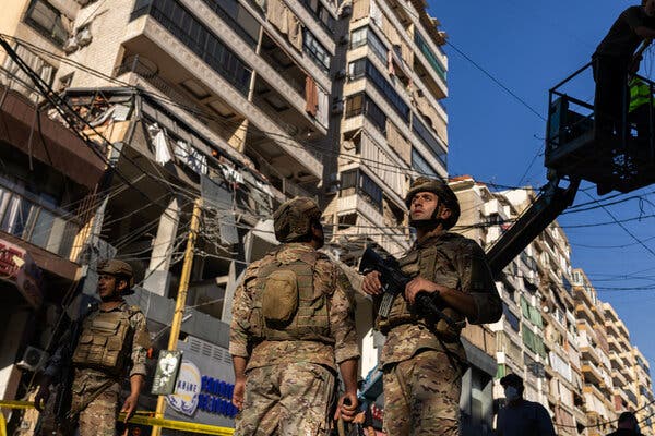 Soldiers stand in front of a damaged building.