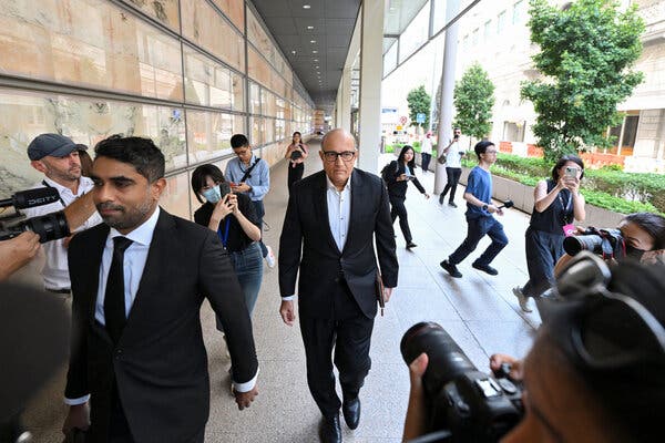 Photographers point their lenses on a man in a suit walking along the side of a building.