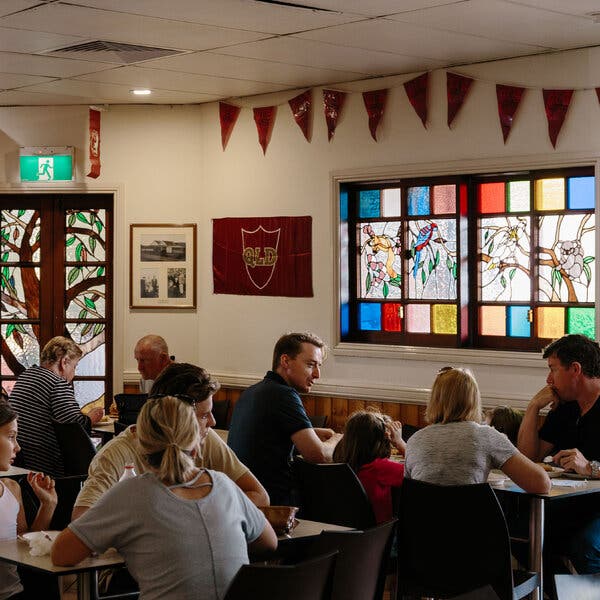 People sit at tables in a room decorated with stained glass windows decorated with koala bears and other Australian themes.