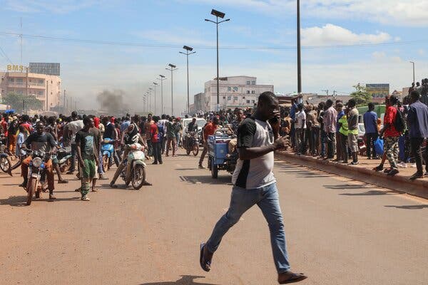 People running on a street as smoke rises in the background. 