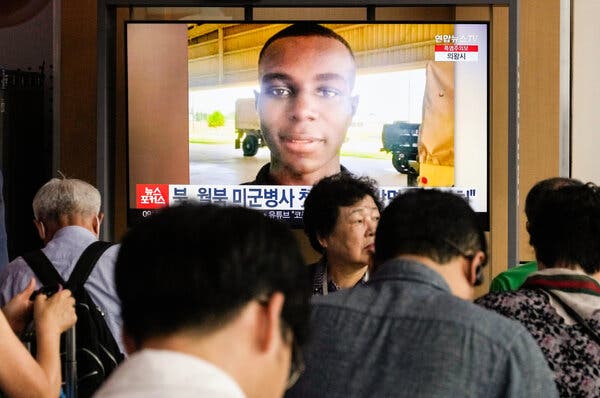 A group of people stand in front of a large flat-screen TV that displays a photo of a young man. 