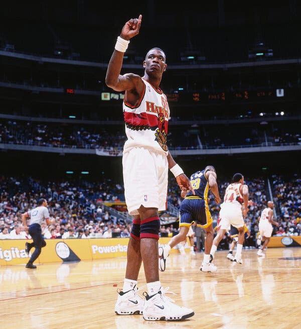 A photo of Dikembe Mutombo on the basketball court raising his right pointer finger in the air.