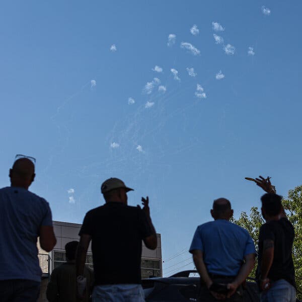 Silhouettes of people looking up in the sky at plumes of smoke.