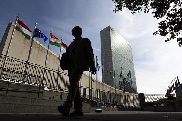 A man walking past a tall building and a row of flags.