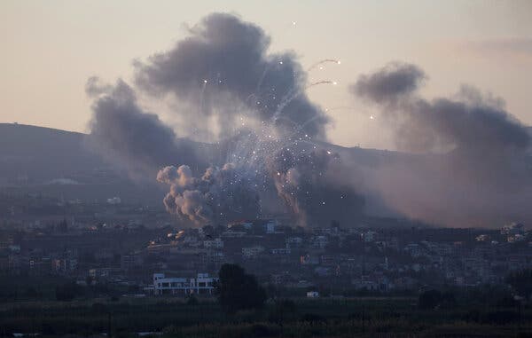 Dark smoke billows and flaming spirals rise in the air over buildings in the distance.