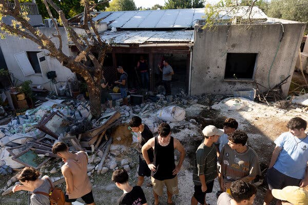 A group of people stand in front of a damage building. Debris covers the ground.