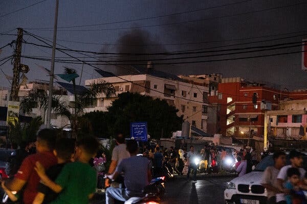 Motorists and pedestrians gather on a street in Beirut. Smoke can be seen in the background. 