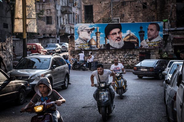 The faces of three men are seen on a large poster on a city street. The middle one has a beard and a black turban.