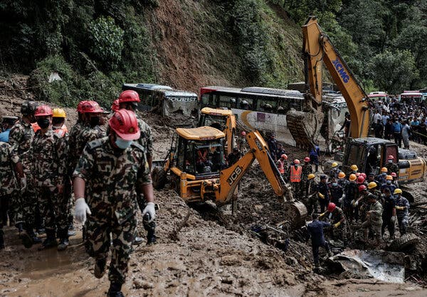 Rescue workers in face masks and helmets work on a mountain in front a two excavators.  