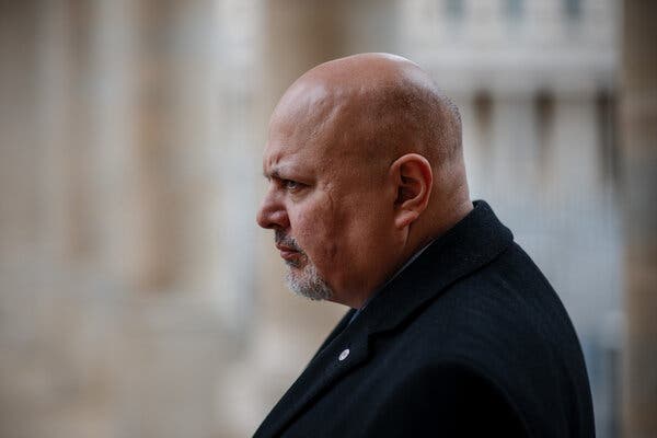 A photo of Karim Khan, who is largely bald and has a graying goatee, from the side. He is wearing black and looks a stern. 