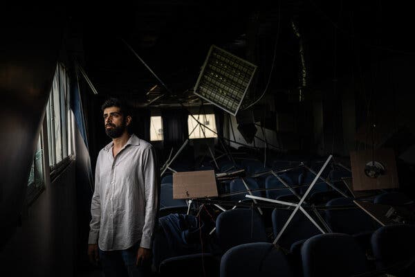 A man with a beard and a long white shirt looks out a window. 