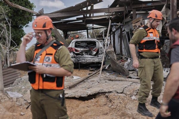 Workers in orange vests and hat at the site where a rocket hit.