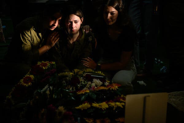 Three people, looking mournful, in a beam of light cutting through a darkened room.