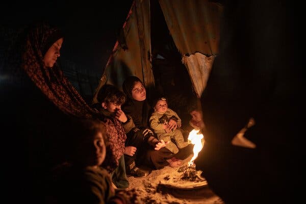 A family trying to keep warm by a fire outside a tent.