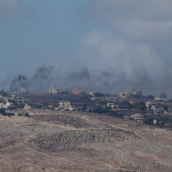 A landscape of buildings on a hillside with smoke rising from the buildings. 