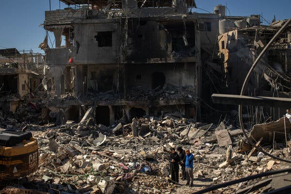 A pile of concrete rubble and twisted metal lies in front of the remains of a bomb-gutted building.