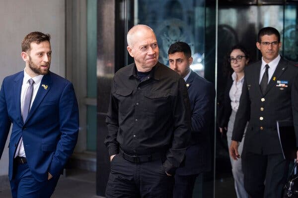 Yoav Gallant, dressed all in black, walks out of the State Department in Washington after meeting with Secretary of State Antony J. Blinken in March. He is smiling and looking to the side. 