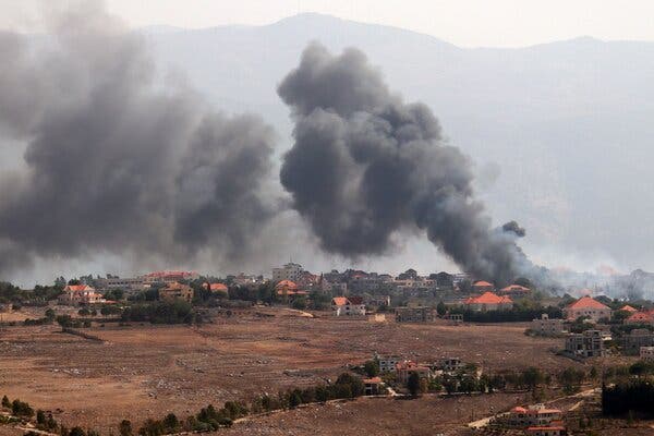 Smoke plumes rise from a small village with mountains in the background.