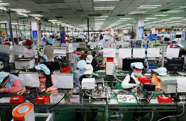 Employees, wearing caps, working at long tables at a Foxconn factory in Zhengzhou, China.  