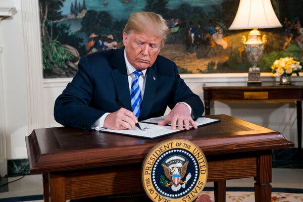 Donald Trump signing a piece of paper while seated at a presidential desk.