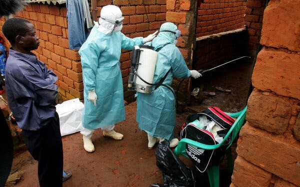 Two people wearing protective medical gear enter a brick building.