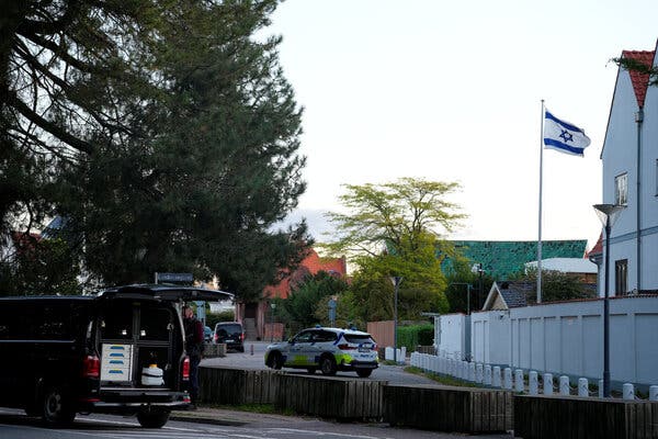 A police car is parked on a street outside of a white building with an Israeli flag flying in front of it. 