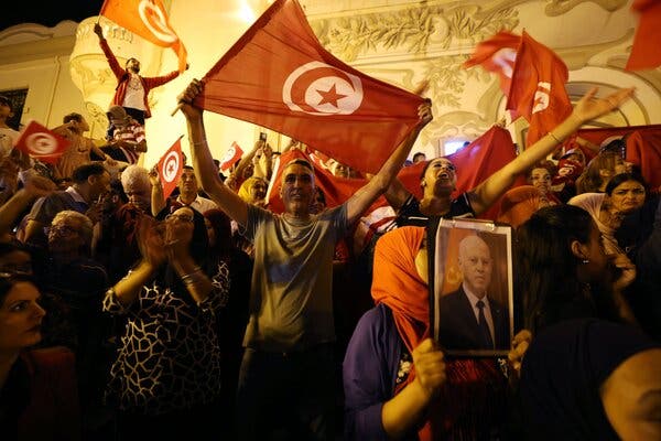 Throngs of people celebrate and wave red Tunisian flags. One holds up a portrait of President Kais Saied.