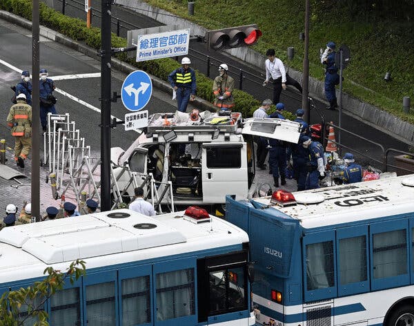 A handful of people mill around a white vehicle that appears to have crashed into a gate. A sign above it reads “Prime Minister’s Office.”