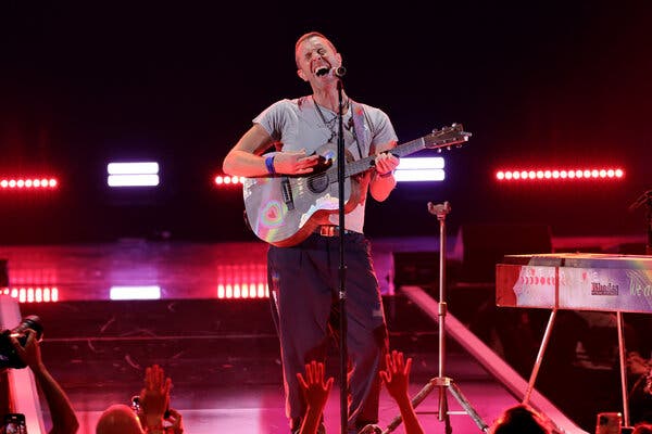 Chris Martin plays a guitar and sings on a neon-lit stage.