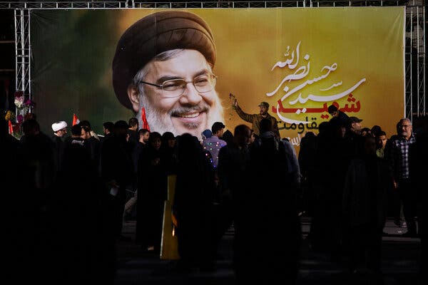 People walk past a large banner of Hassan Nasrallah.