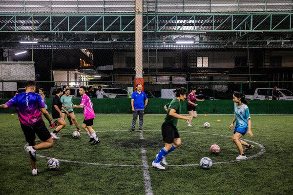 A coach watches on as soccer players practice on a field.