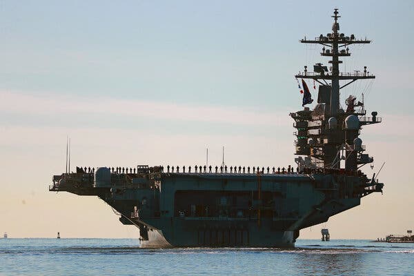 Sailors and Marines line the deck of an aircraft carrier.