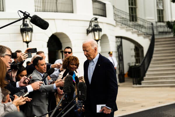 President Biden stands before a cluster of reporters and photographers with the White House in the background.