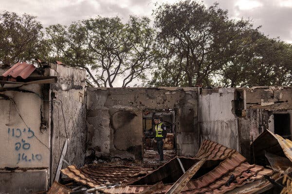 A man in a neon yellow vest stands amid the rubble of a home.