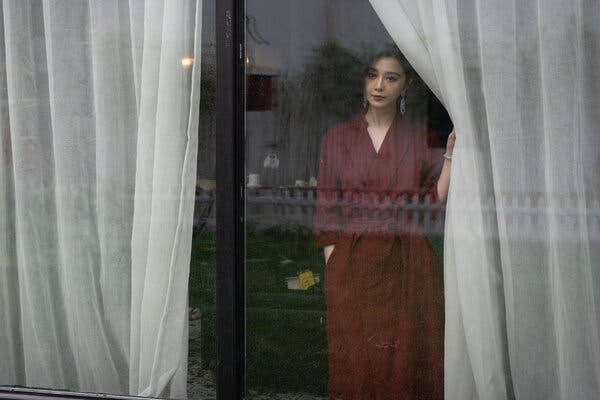 A woman in a red dress stands behind a glass window.