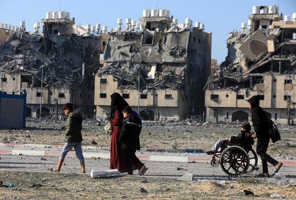 People walking on a road and in the background among destroyed buildings.