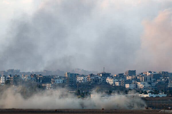 A military vehicle kicking up a large cloud of dust, with many buildings visible in the background.